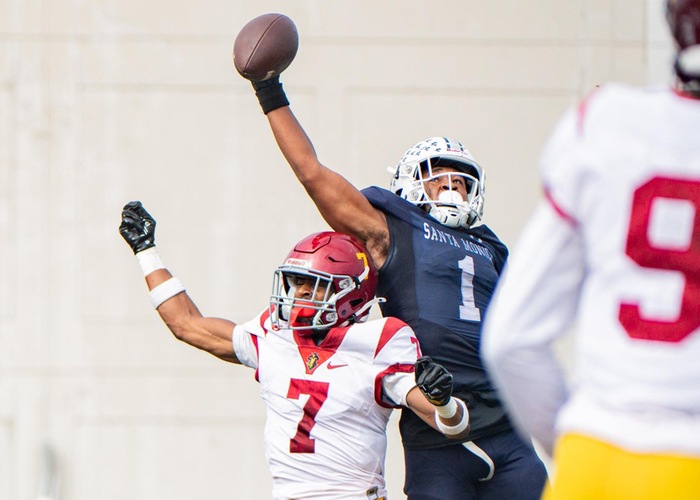 football player in blue jersey reaching for a pass against a defender
