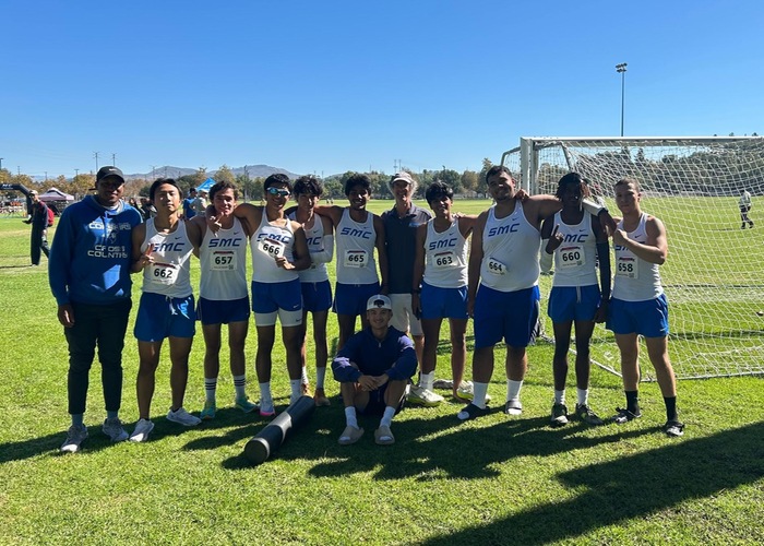 Cross Country team in white jerseys smiling in a group photo after their races.