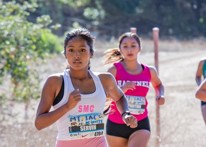 female runner in white jersey running along a dirt path