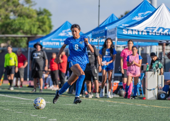 Santa Monica female soccer player runs down a turf field with the ball.