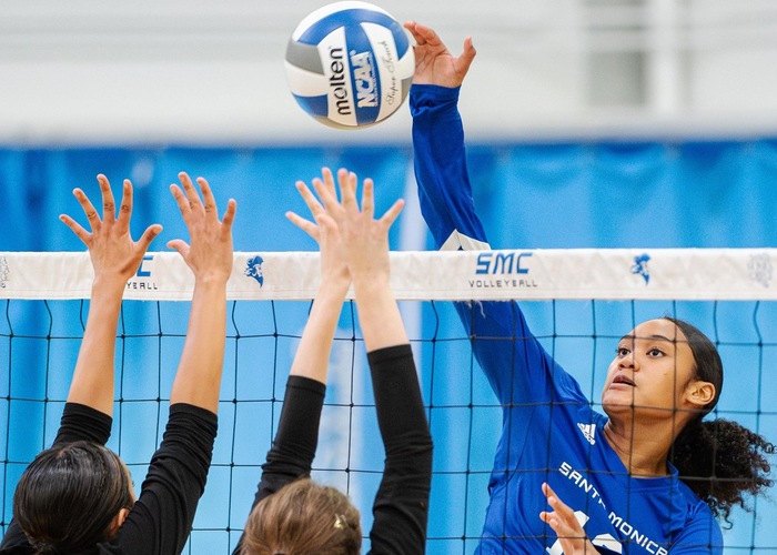 female volleyball player in blue jersey spikes the ball over the net